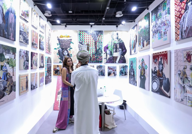 Artist discussing artwork with a visitor at an exhibitor booth during World Art Dubai