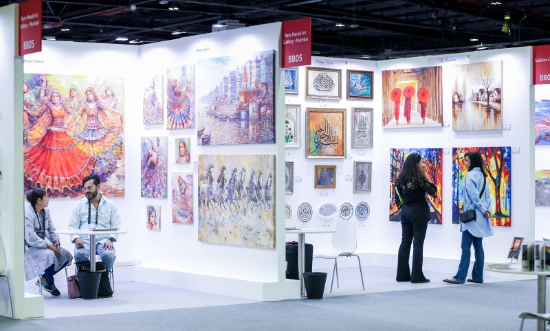 Artist presenting paintings at a structured booth during World Art Dubai exhibition